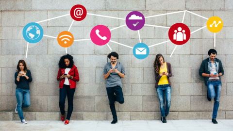 people standing against a brick wall looking down at their phones