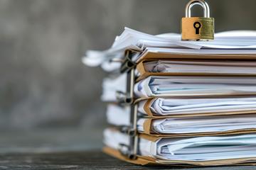 stack of folders containing files with a metal padlock on top pile