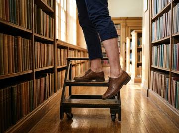 Person standing on wooden step stool in library