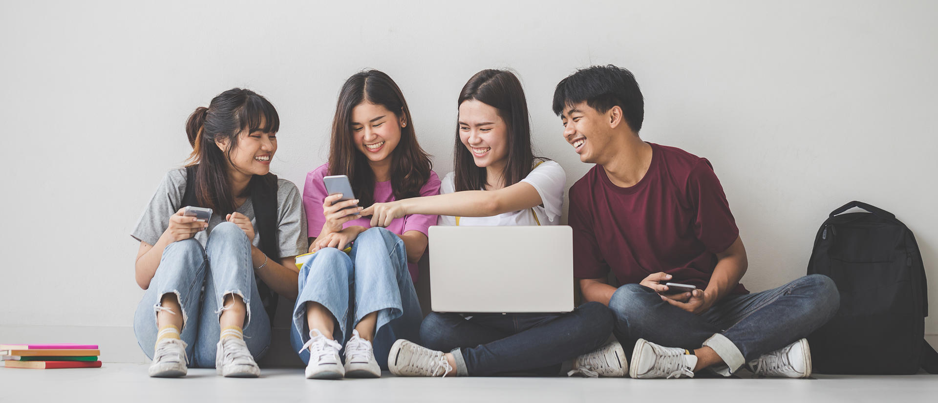 cheerful students sitting on floor gathered around a laptop